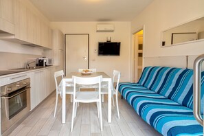 A compact kitchen with a dining table, chairs, a sofa, and a TV.