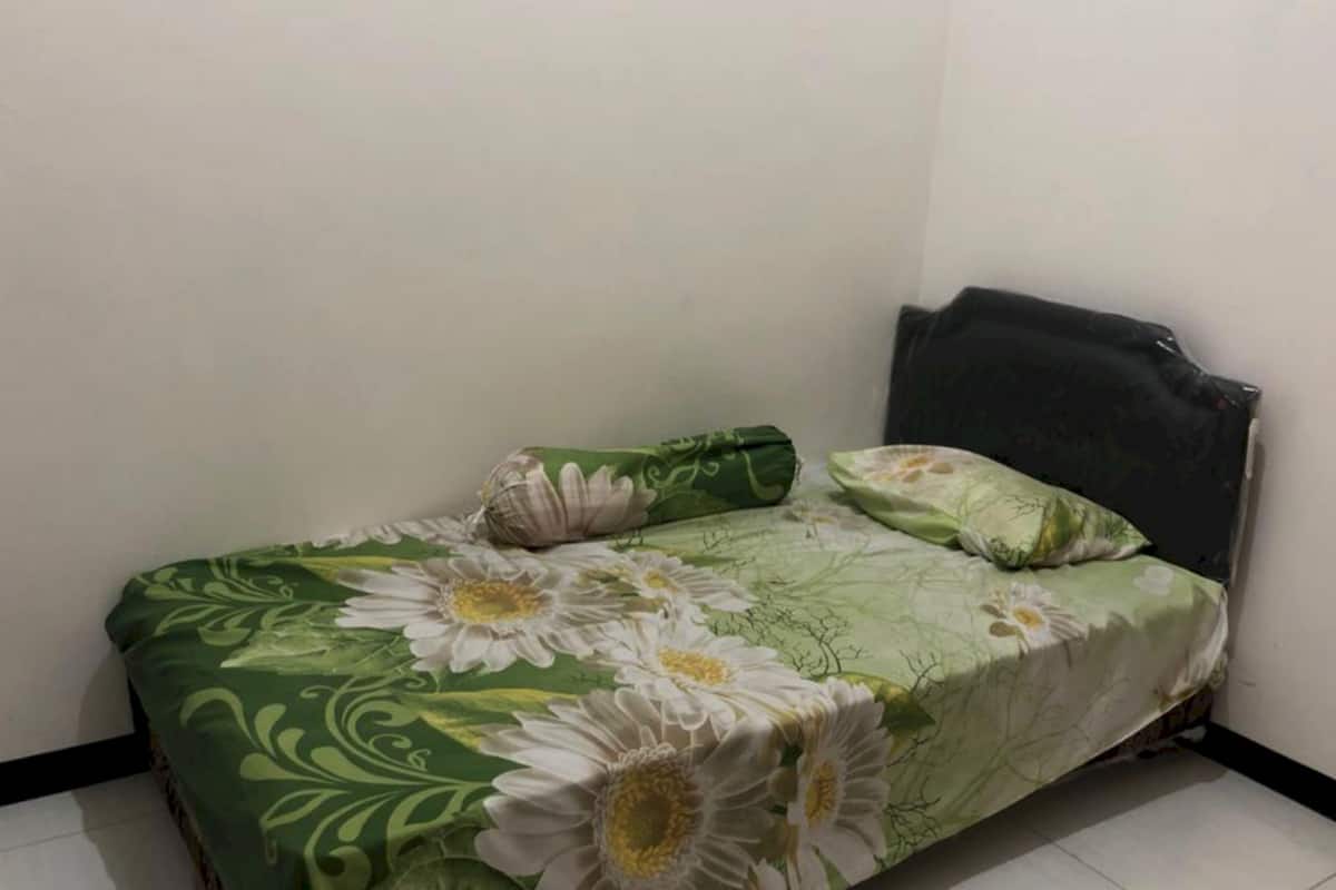 A small, single-bed room with a floral bedspread, a green pillow, and a dark headboard.