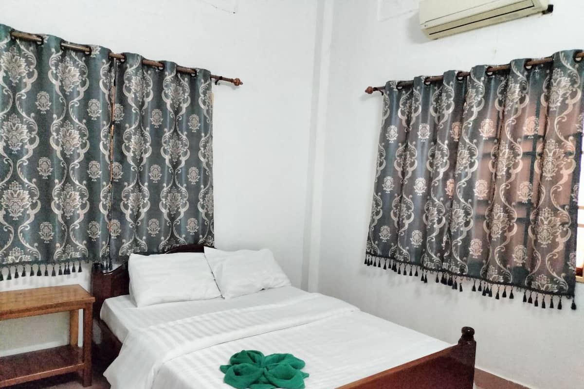 A single-bed room with a wooden headboard, white bedding, and a green towel on the bed.