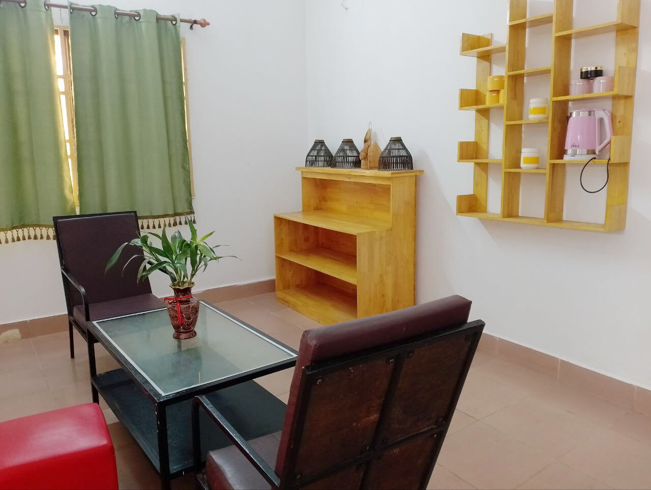 A dining area with a glass table, chairs, a wooden shelf with kitchen items, and a green curtain.