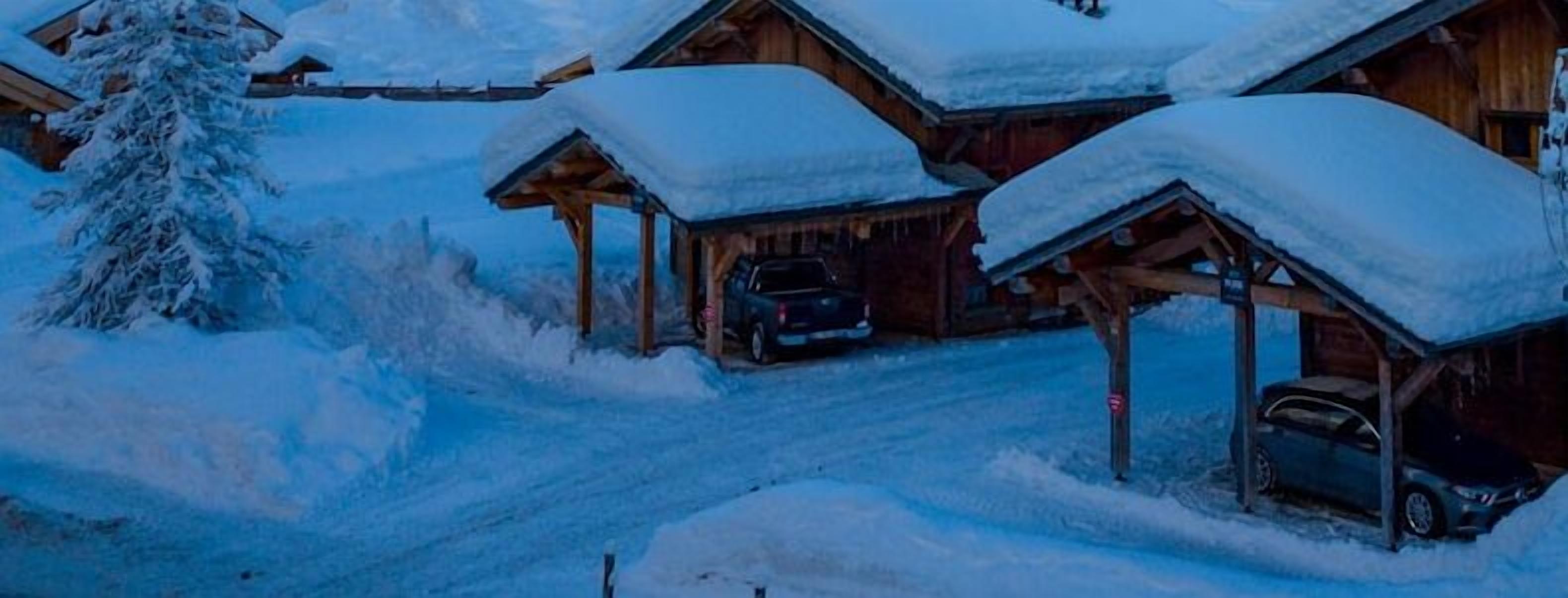 Eine schneebedeckte Lodge mit mehreren Holzhütten, vor jeder Hütte ein geparktes Auto.