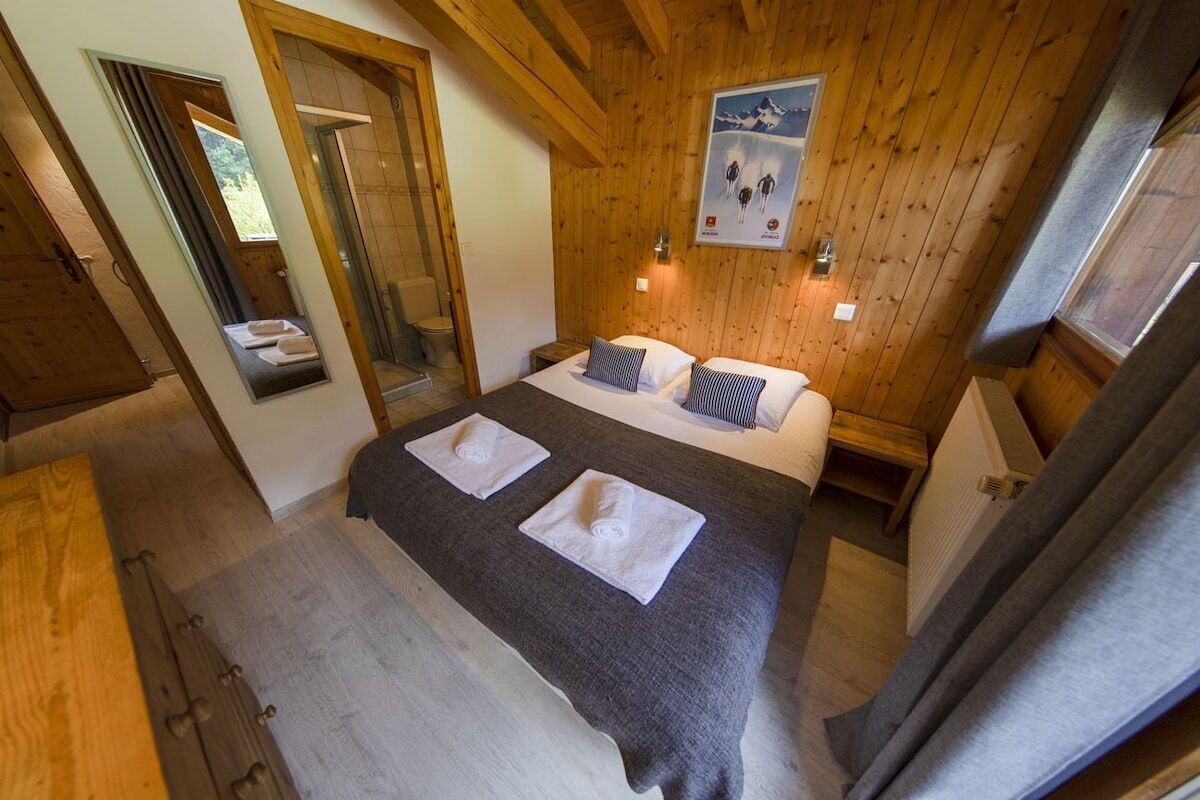 A bedroom with a wooden ceiling, a bed with two pillows, a nightstand, and a mirror.