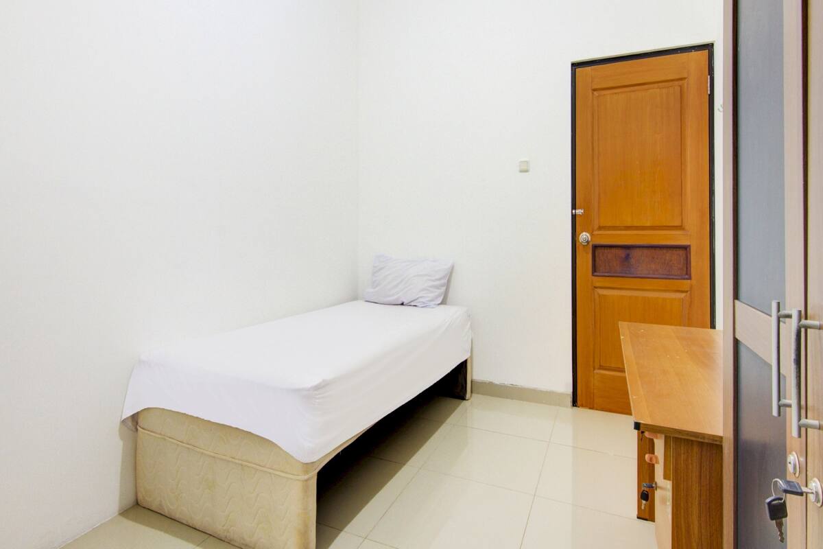 A small, single-bed room with a wooden door and a small wooden cabinet.