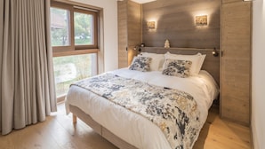 A bedroom with a large bed, wooden headboard, and a window with curtains.