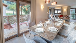A dining area with a long table set for six, large windows, and a view of the outdoors.