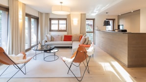 A modern living room with a sofa, two armchairs, a coffee table, and a dining area with a counter.