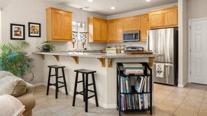 A kitchen with wooden cabinets, a stainless steel refrigerator, a microwave, and a small island with stools. - A fresh new offering - Welcome to your Chico Getaway! (Chico)