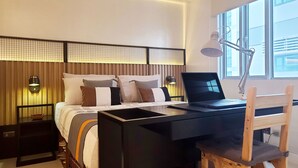 Een moderne slaapkamer met een bed, een bureau en een stoel. Twee wandlampen en een raam met jaloezieën.
