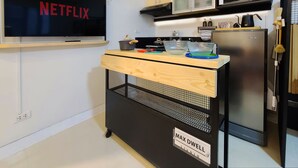 Een moderne keuken met een televisie waarop 'NETFLIX' wordt weergegeven, een magnetron, een koelkast en een houten kar met de tekst 'MAX DWELL STUDIO'.