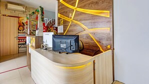 A reception desk with a wooden finish and a modern design, featuring a built-in air conditioning unit and a small decorative item on top. - OYO Dupak Inn (Surabaya)