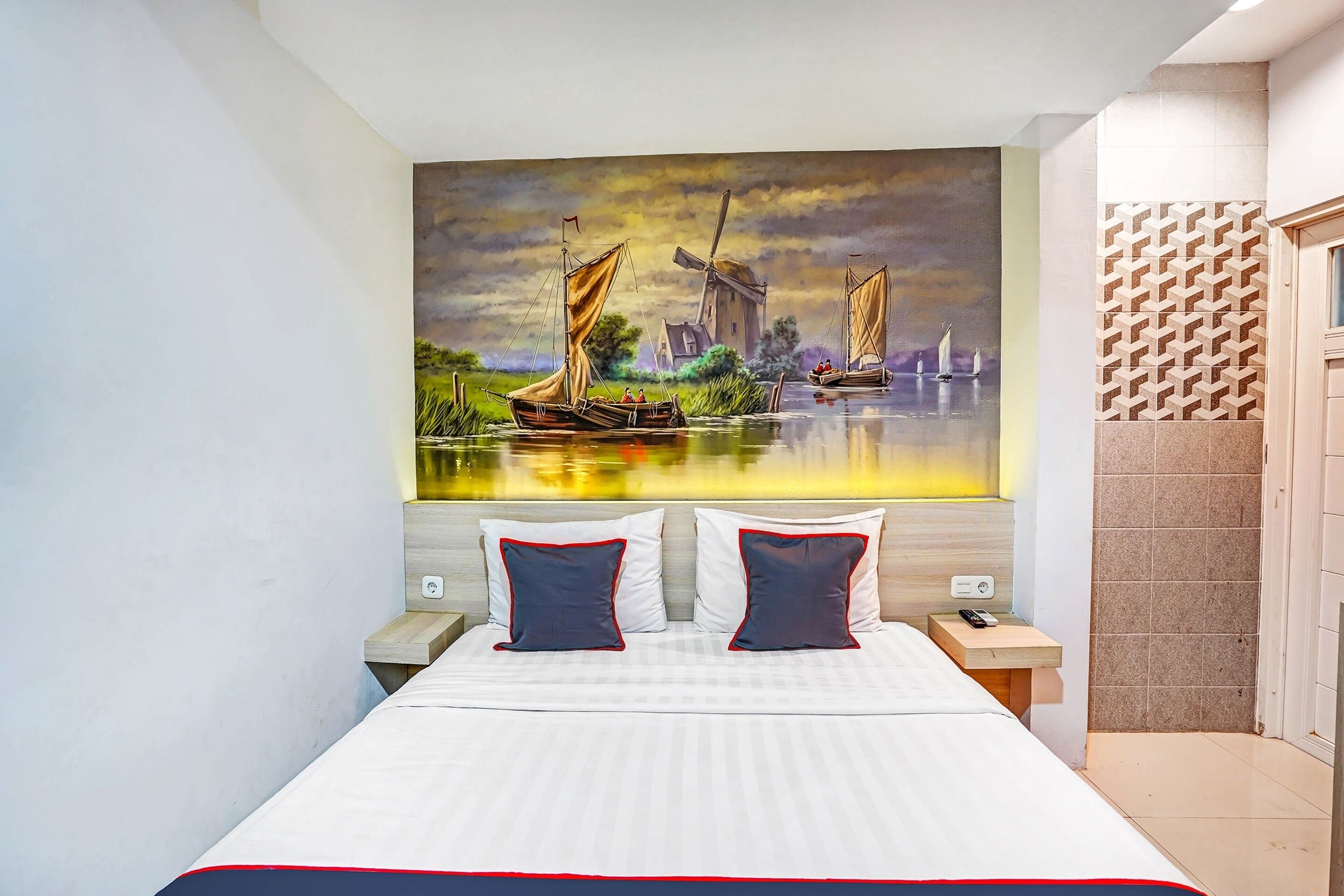 Een slaapkamer met een bed, twee kussens, een nachtkastje, een aan de muur hangend schilderij van een landschap en een behang met patroon.