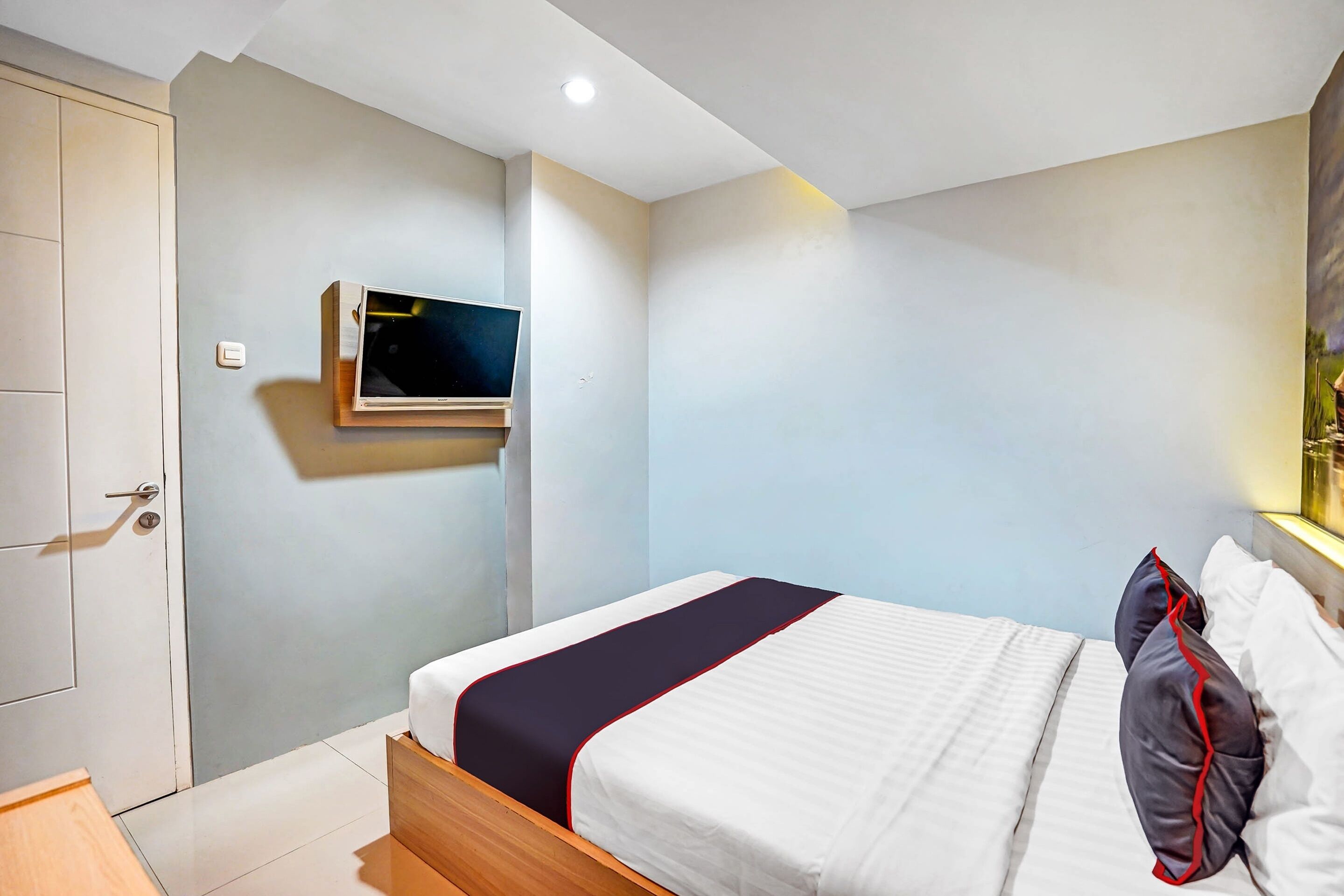 A hotel room with a bed, a television mounted on the wall, and a door.