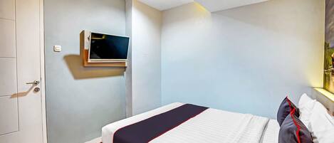 A hotel room with a bed, a television mounted on the wall, and a door.
