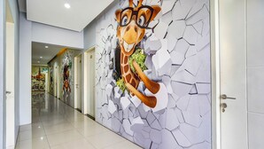 A hallway with a mural of a giraffe breaking through a wall, leading to a door. - OYO Dupak Inn (Surabaya)