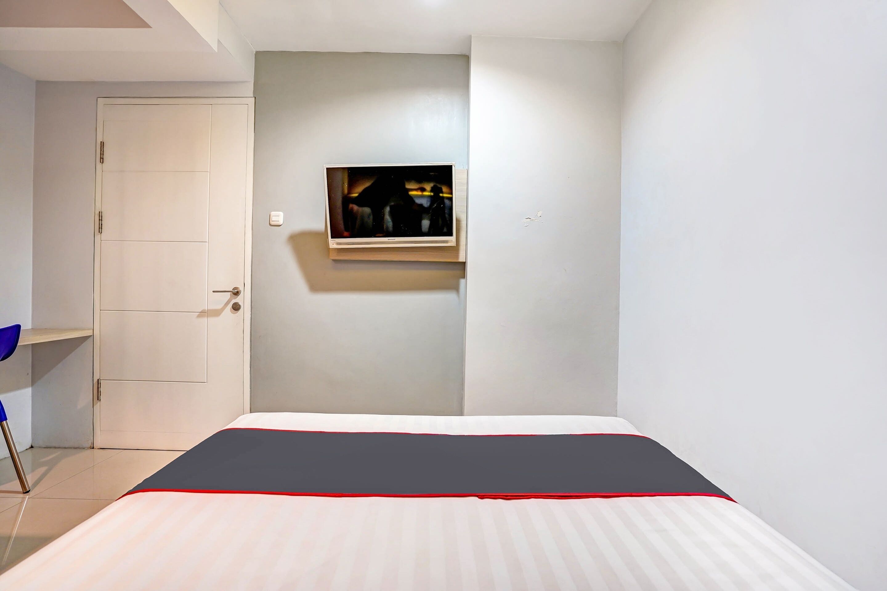 Un dormitorio con cama, una puerta, una pequeña estantería y un cuadro colgado en la pared.
