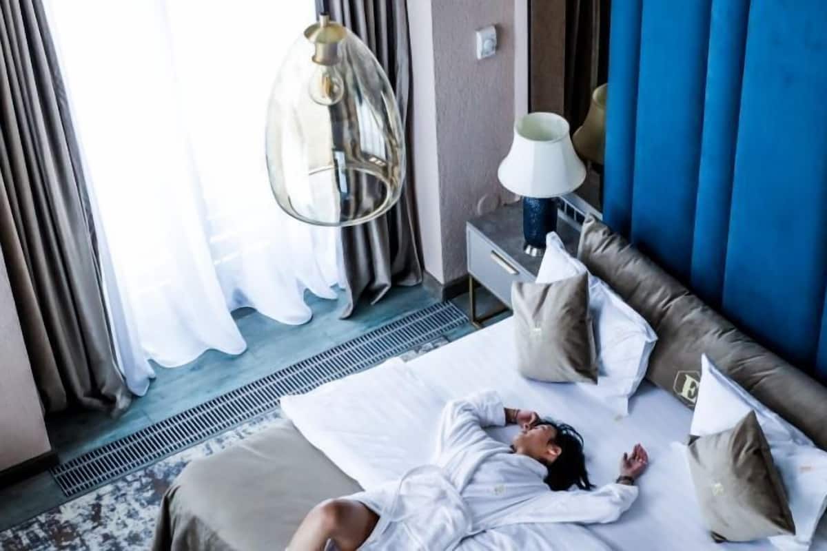 Une chambre d’hôtel avec un lit, des oreillers, une table de chevet avec une lampe et une fenêtre avec des rideaux.