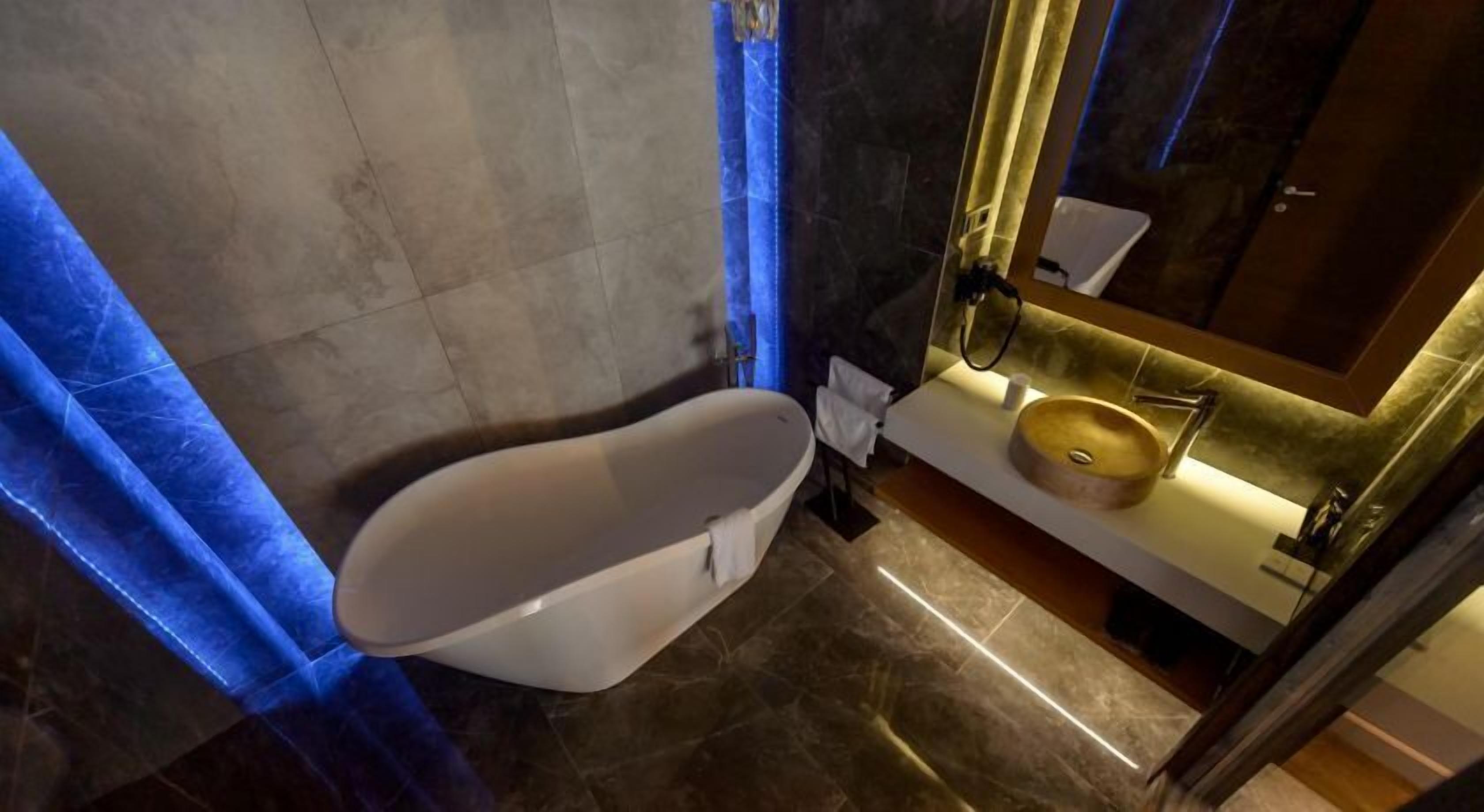 A modern bathroom with a freestanding bathtub, a round sink, and a mirror with a gold frame.