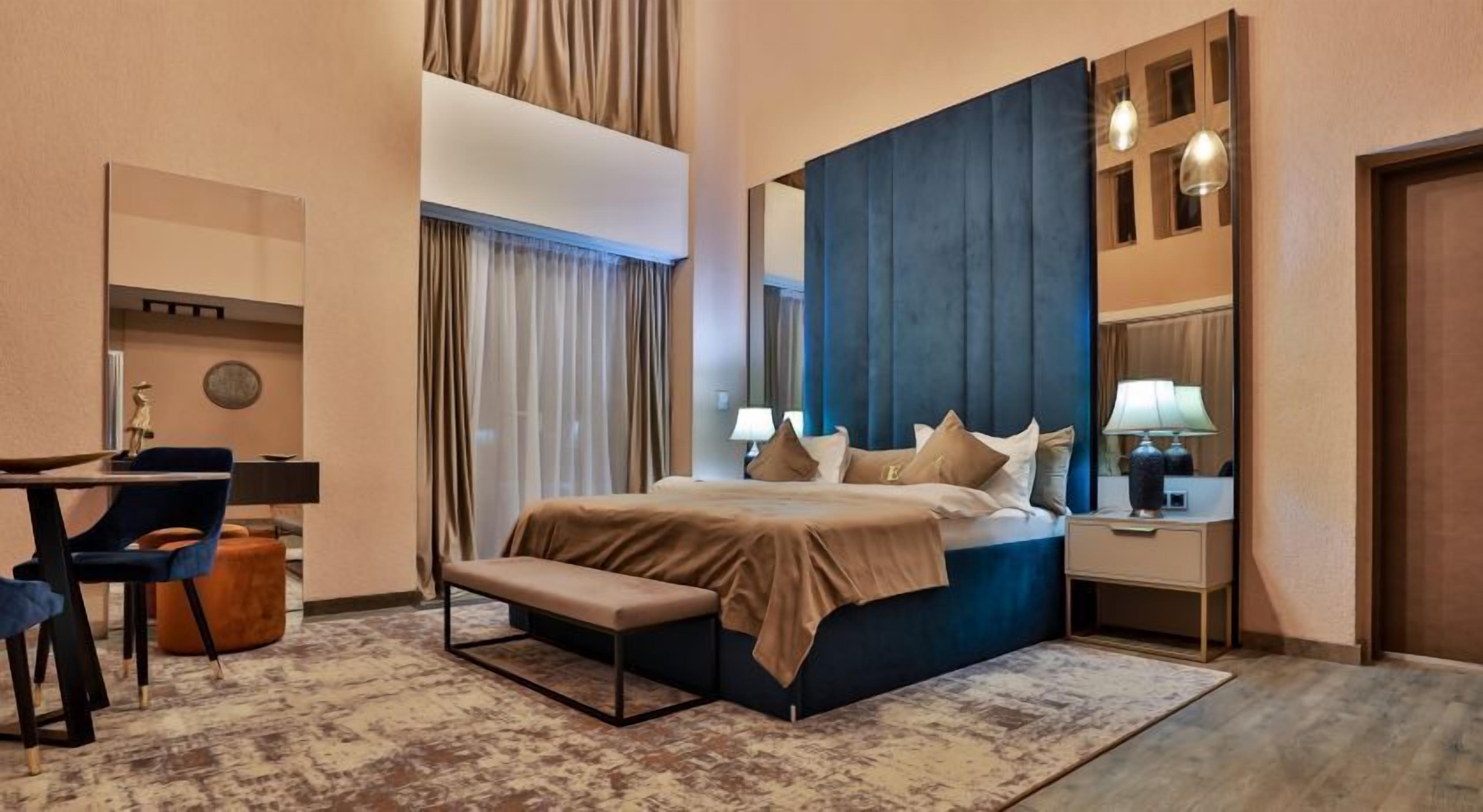 Une chambre d’hôtel comprenant un lit, une table de chevet, une lampe, une chaise et un bureau avec une autre chaise.