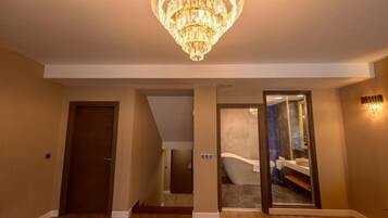 A hallway with a chandelier, a door, and a bathroom visible through a glass door.
