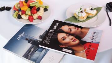 Een tafel met diverse gerechten, waaronder fruit en gebak, en een tijdschrift met de titel 'Forbes Woman'.