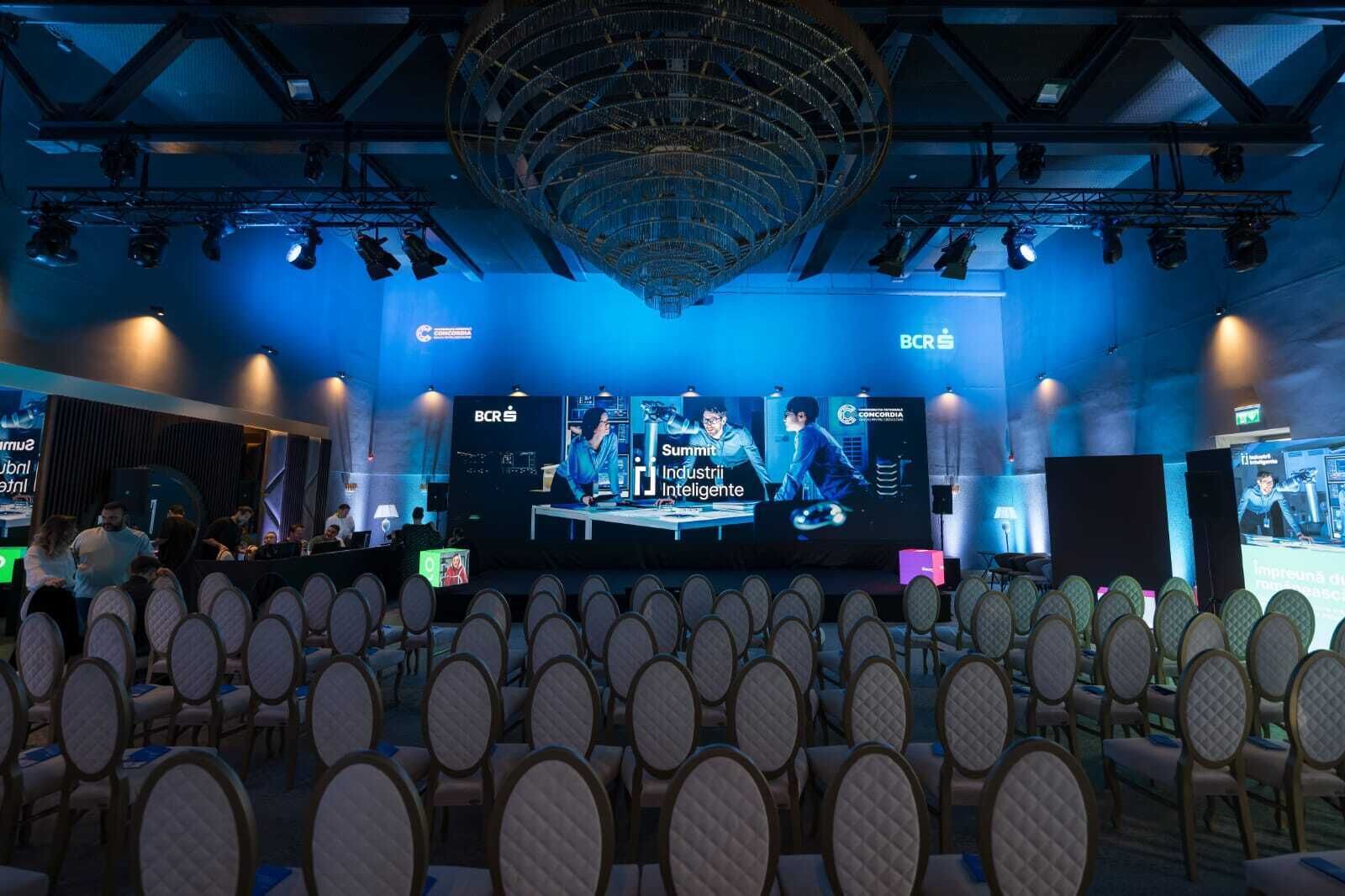 A conference room with rows of chairs facing a stage with a large screen displaying a presentation.