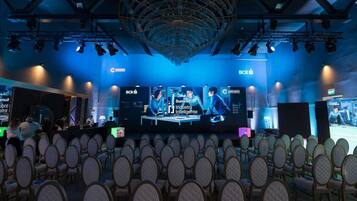 A conference room with rows of chairs facing a stage with a large screen displaying a presentation.