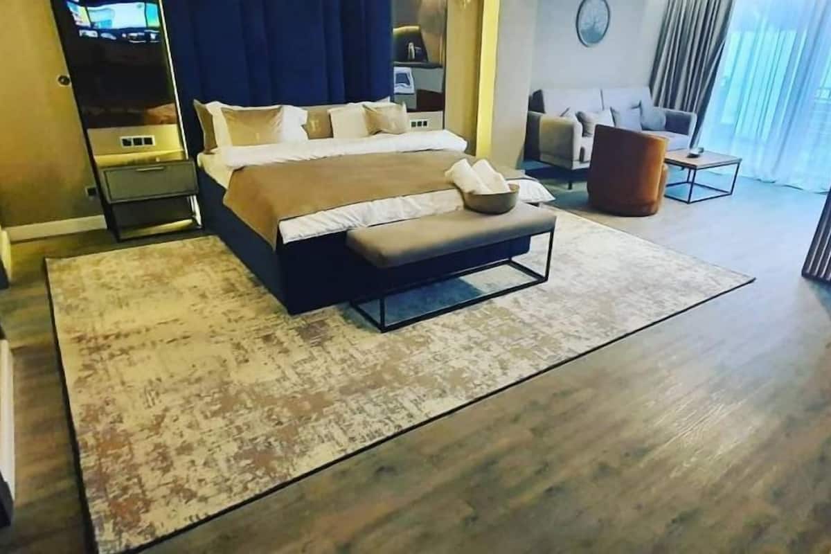 Une chambre d’hôtel moderne avec un grand lit, une banquette, un canapé et une vue sur l’extérieur.