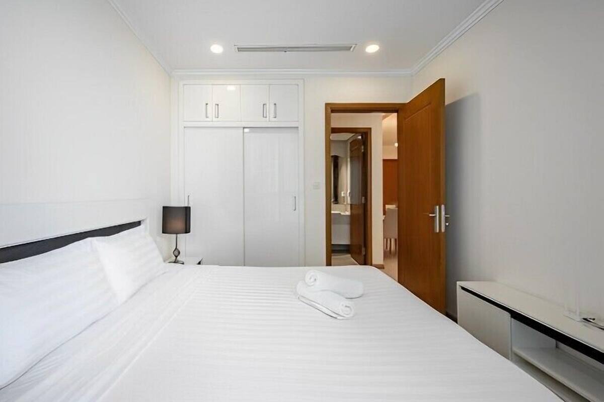 A hotel room with a bed, a bedside lamp, a wardrobe, and a bathroom visible through an open door.