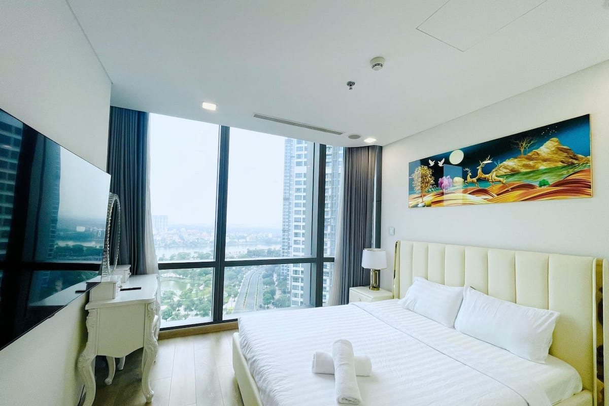 A hotel room with a large bed, a desk, a chair, a TV, and a painting on the wall.