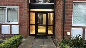 A building entrance with a glass door, brick walls, and a small garden area. - Lady Jane Court (Cambridge)