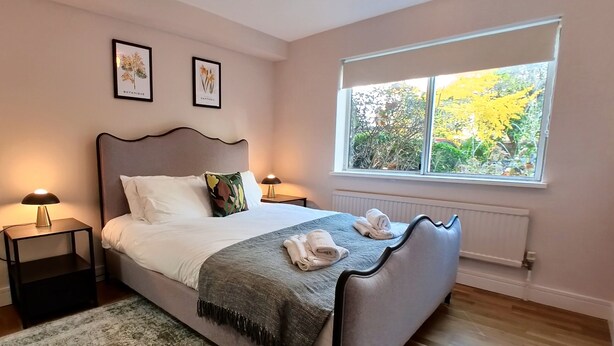 A bedroom with a bed, two nightstands, a window with a view of trees, and two framed botanical prints on the wall. - Lady Jane Court (Cambridge)