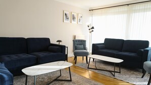 A modern living room with two dark sofas, a light-colored coffee table, and a grey armchair. - Lady Jane Court (Cambridge)