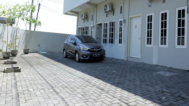 Un coche aparcado en un camino de entrada pavimentado frente a un edificio con varias ventanas y unidades de aire acondicionado.