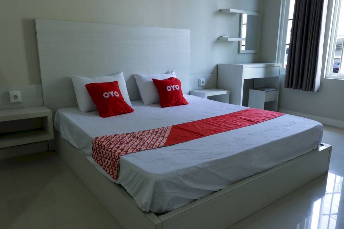 A modern hotel room with a large bed, white bedding, and red pillows.