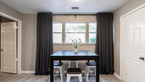 A dining area with a table and two chairs, a window with curtains, and a door. - 2BR The Cardinal C! Montrose, Downtown MedCenter ⭐️⭐️⭐️⭐️⭐️ (Houston)