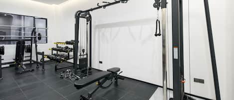 Un gimnasio con varios equipos de ejercicio, incluyendo una banca, mancuernas y una estructura para sentadillas.