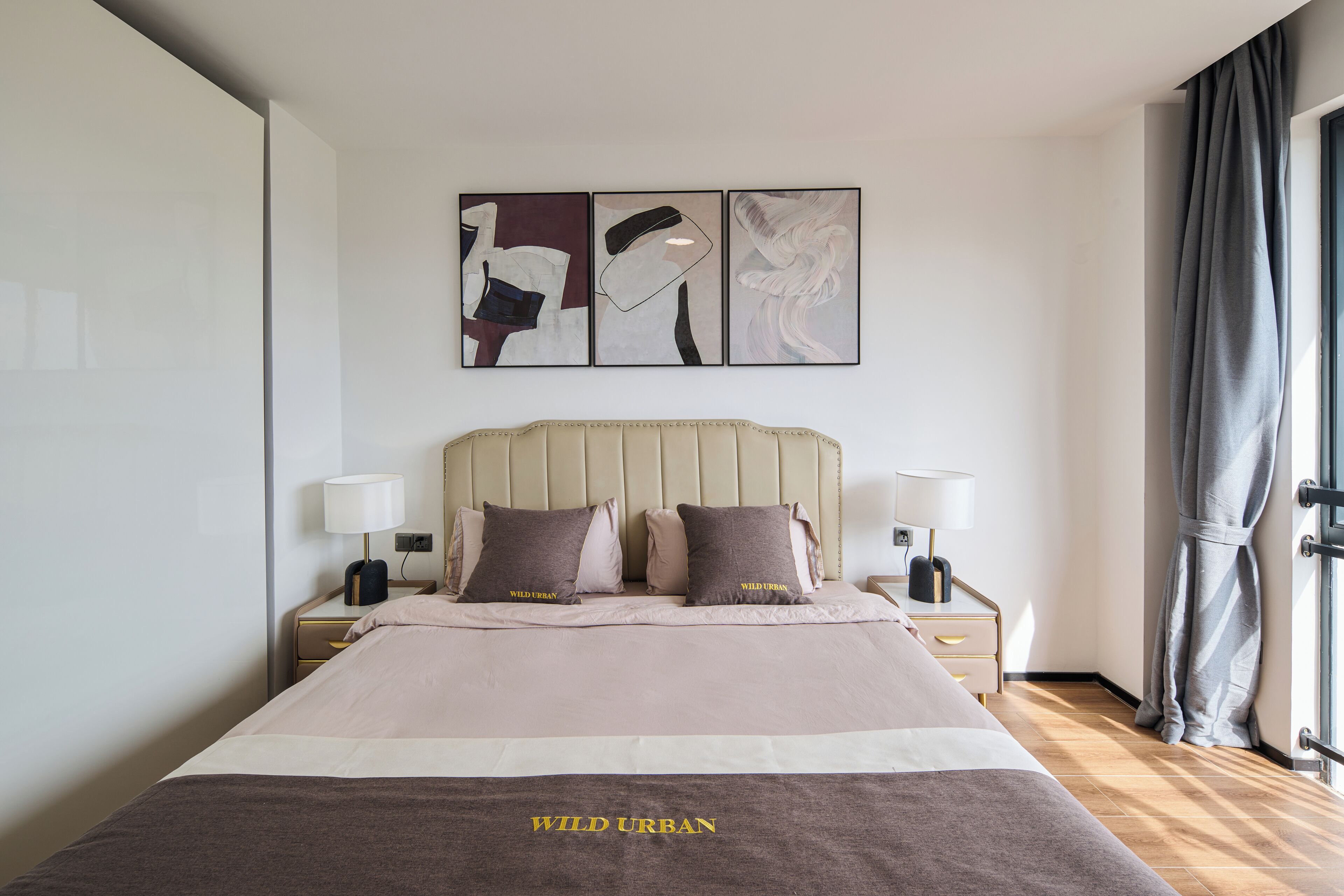 A hotel room with a large bed, two bedside tables, a headboard, and a window with curtains.