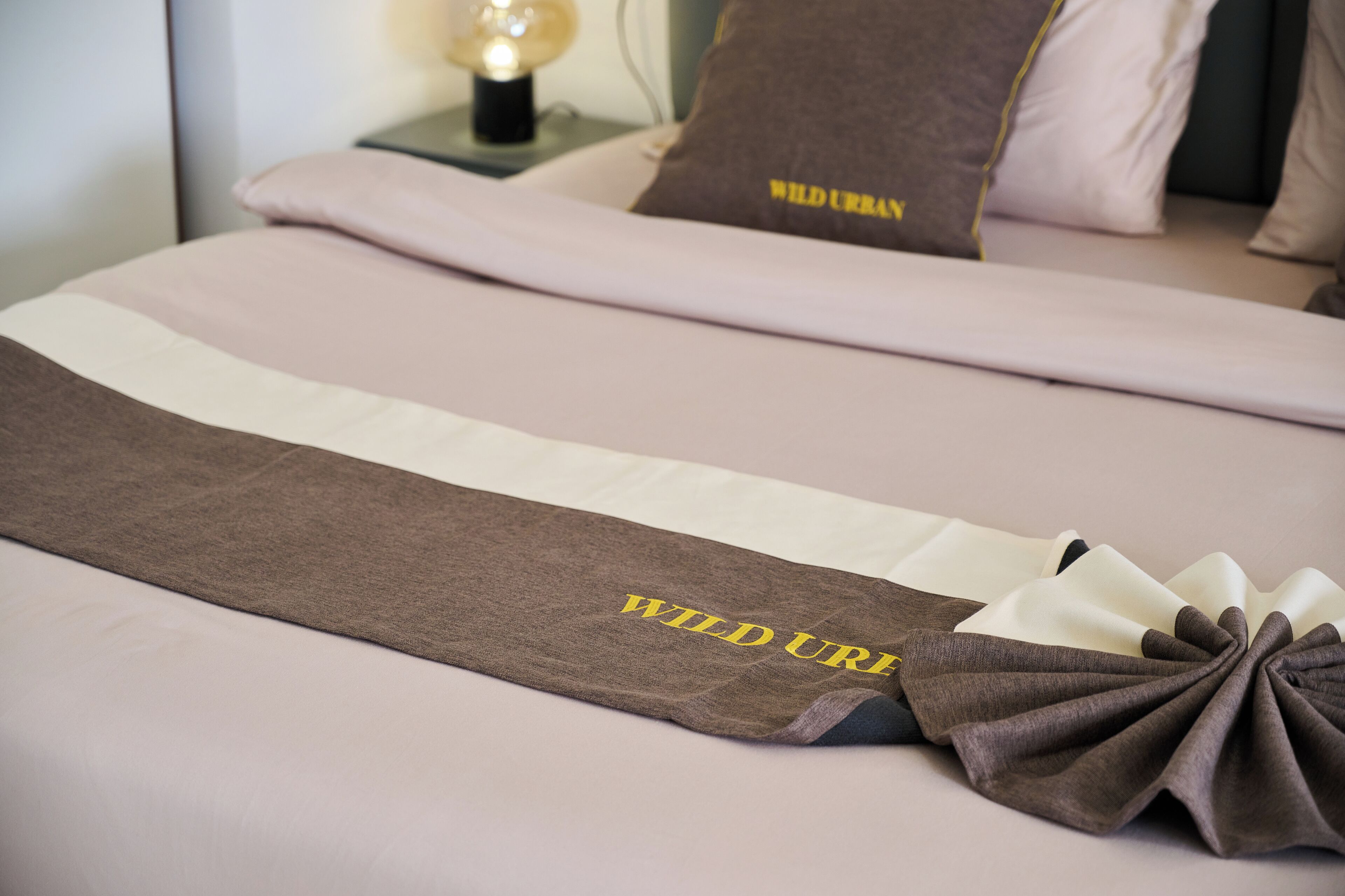 A neatly made bed with a brown and white striped bedspread and a decorative pillow with "WILD URBAN" text.