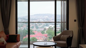 A modern living room with a large window, a sofa, a chair, and a small table with two glasses. - Oasis Park (Kigali)