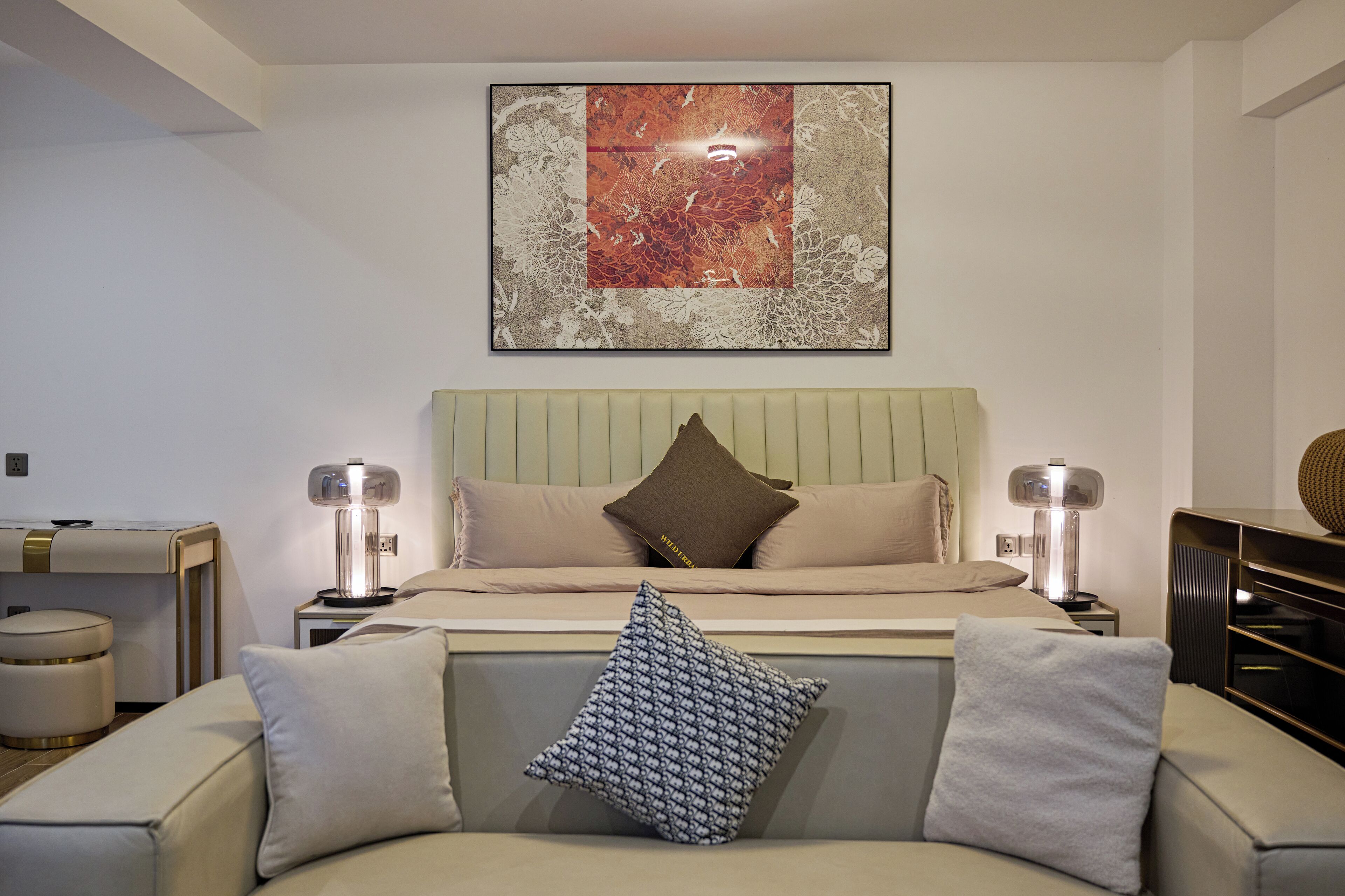 A modern bedroom with a bed, two bedside tables, a nightstand, a sofa, and a wall-mounted artwork.
