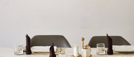 A dining area with a table set for two, a framed artwork of a deer, and a modern light fixture above.