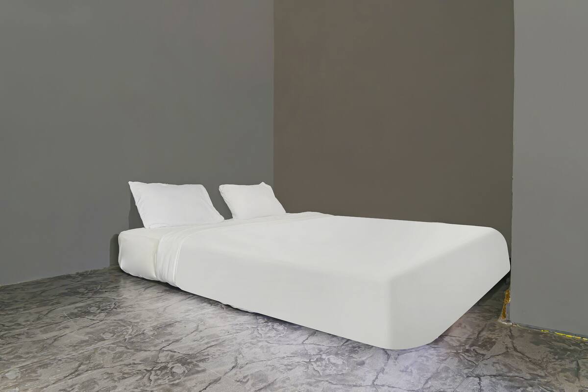 Een bed met wit beddengoed in een kamer met een marmeren vloer en effen muren.