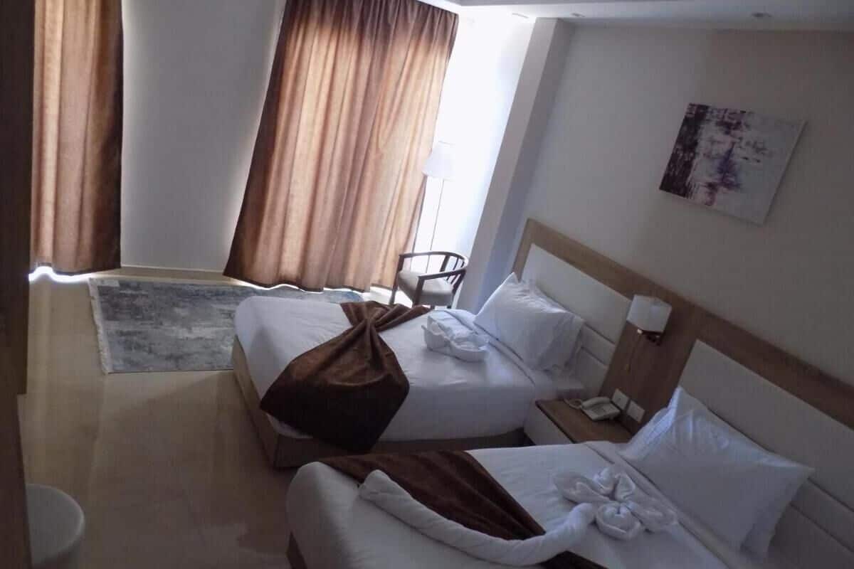 A hotel room with two beds, a small table, a chair, a lamp, and a painting on the wall.