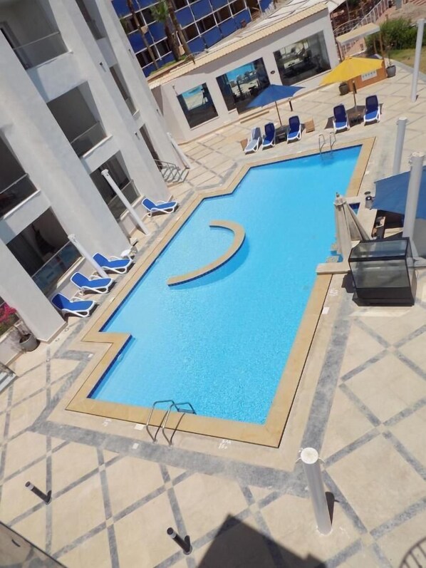 An outdoor swimming pool with blue water, surrounded by lounge chairs and umbrellas.