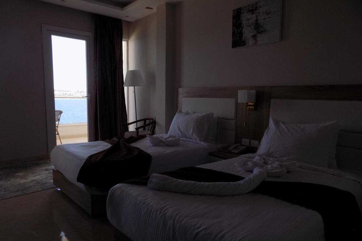 A hotel room with two beds, a large window with a view of the sea, and a chair by the window.