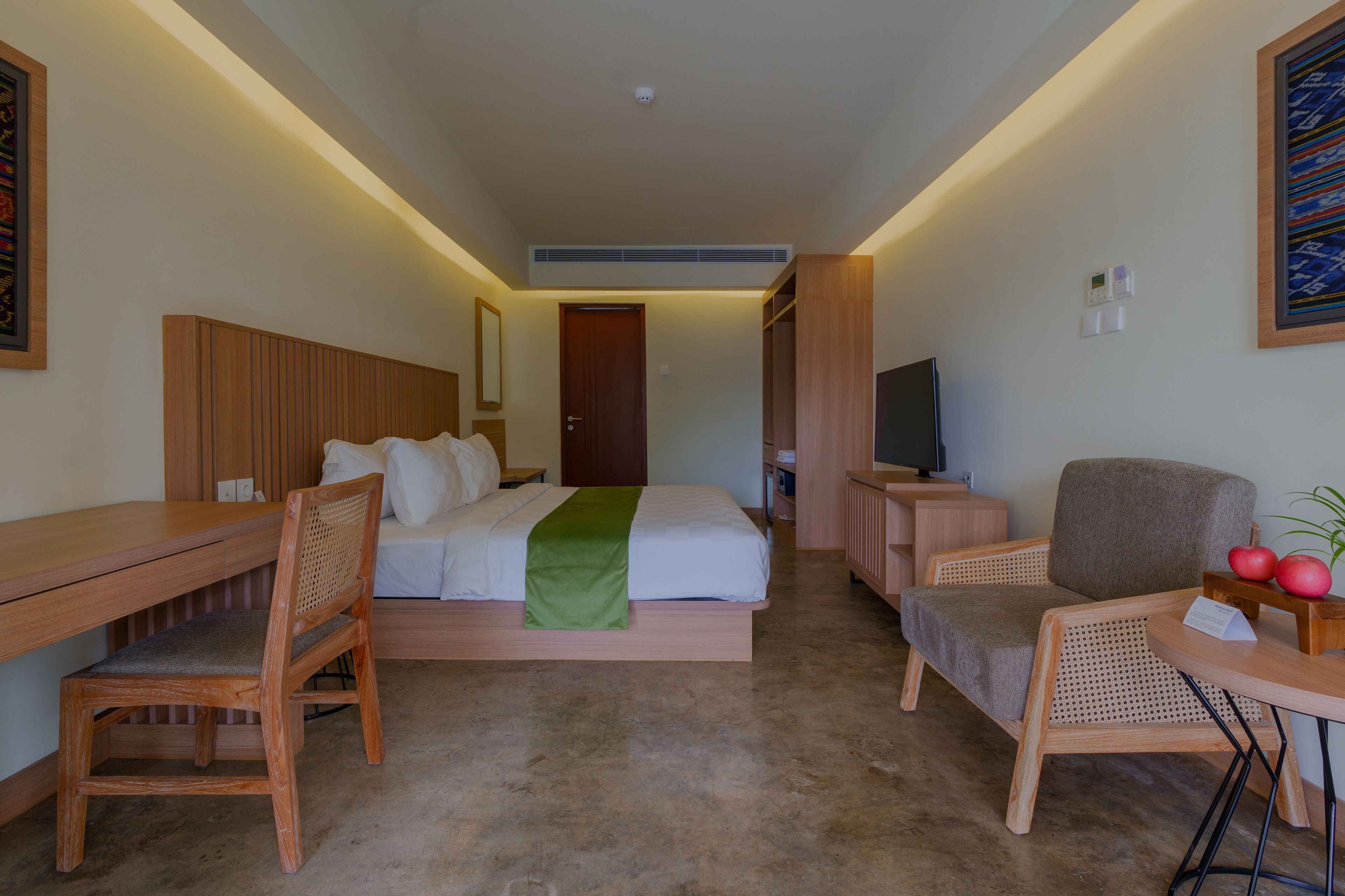 Una camera d'albergo con un letto, una scrivania, una sedia, una TV e un piccolo tavolo con frutta.