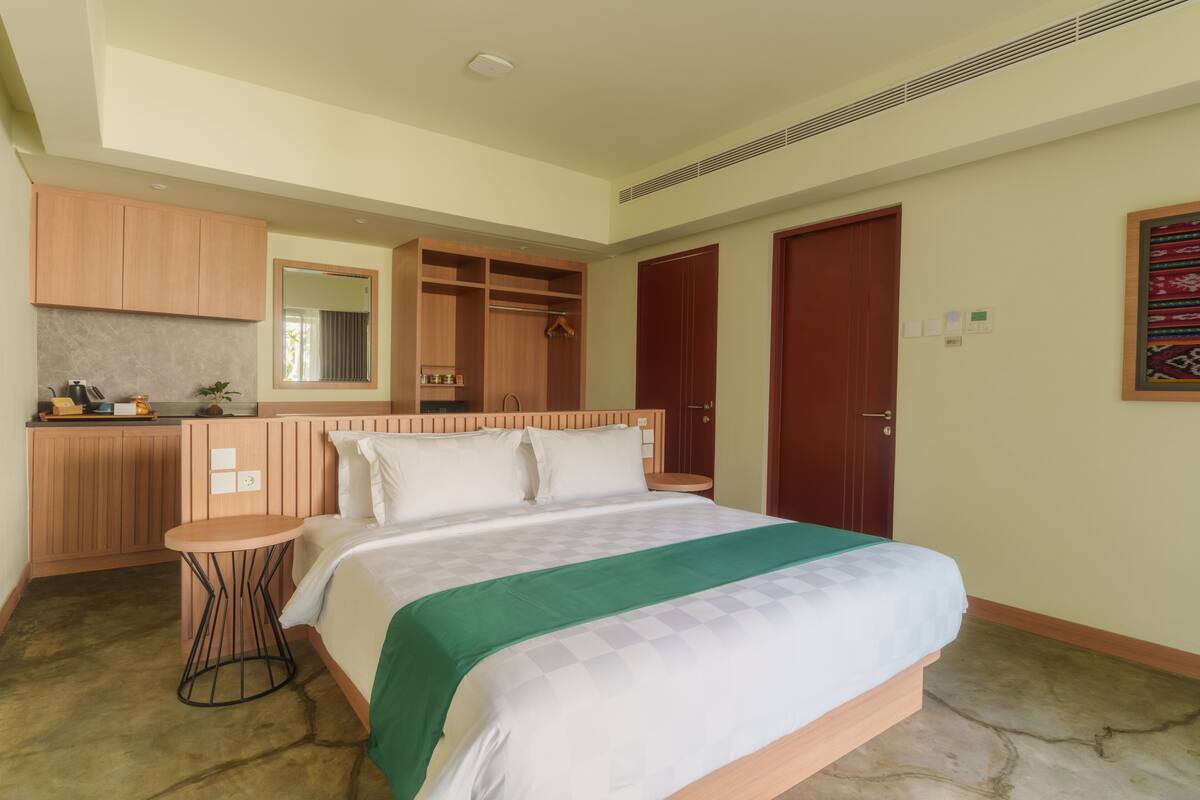 Quarto com cama, uma mesinha redonda, guarda-roupa de madeira e espelho.