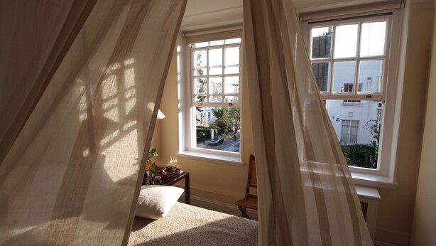 A bedroom with a bed, a chair, a window, and curtains. - Luxury Apartment in Chelsea (London)