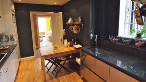 A modern kitchen with wooden flooring, a black countertop, and stainless steel appliances. There is a window with a view of the outside, and a door leading to another room. - Luxury Apartment in Chelsea (London)