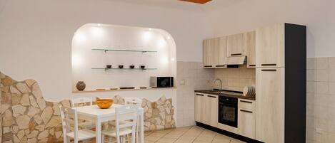 Una cocina moderna con armarios blancos, una pared de acento de piedra y un área de comedor con sillas blancas y un bol.